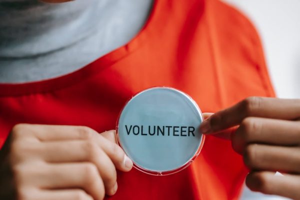 Close-up of a smiling volunteer holding a badge in a bright setting.